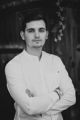 A man stands with his arms crossed, wearing a white shirt