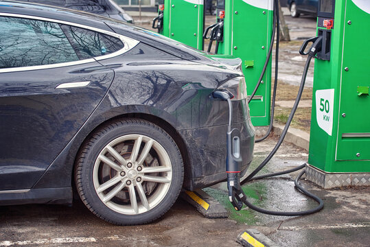 Minsk, Belarus. Feb 4, 2024.  Tesla Model S parked at parking lot and charge battery at electric charge point, electric car charging in cold winter season. Charging EV car, side view