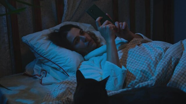 Insomnia. Young woman can't fall asleep at night. Sleepless woman lying in bed with smartphone in her hands.