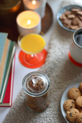 Cup of tea or coffee, stack of books, e-reader, glasses, various cookies, almonds, orange juice and lit candles on the table. Hygge at home. Selective focus.