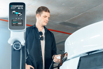 Young man travel with EV electric car to shopping center parking lot charging in downtown city...