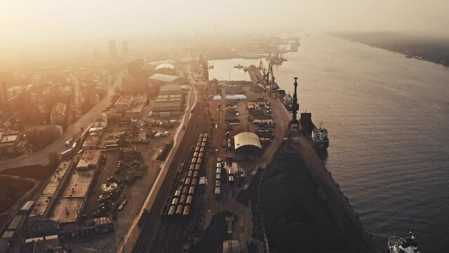 Aerial view. Railway sorting station at sunset. Many wagons and railway tracks at industrial freight station. Train along the tracks. Heavy industry landscape. City port zone. Ships, cargo in seaport