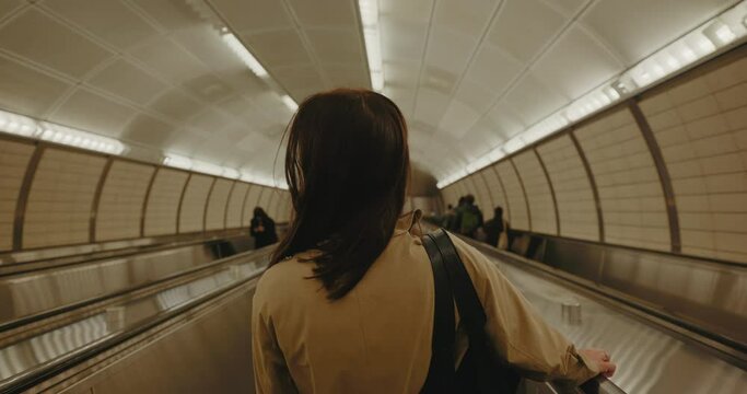 Rear view of brunette female tourist riding the escalator down to the subway.