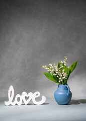 A small bouquet of white flowers, lilies of the valley in a blue vase next to the inscription...