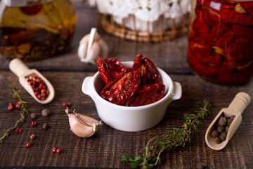 Sun-dried tomatoes in olive oil in a white bowl with pepper, garlic and thyme in a rustic style. Selective focus, close-up.