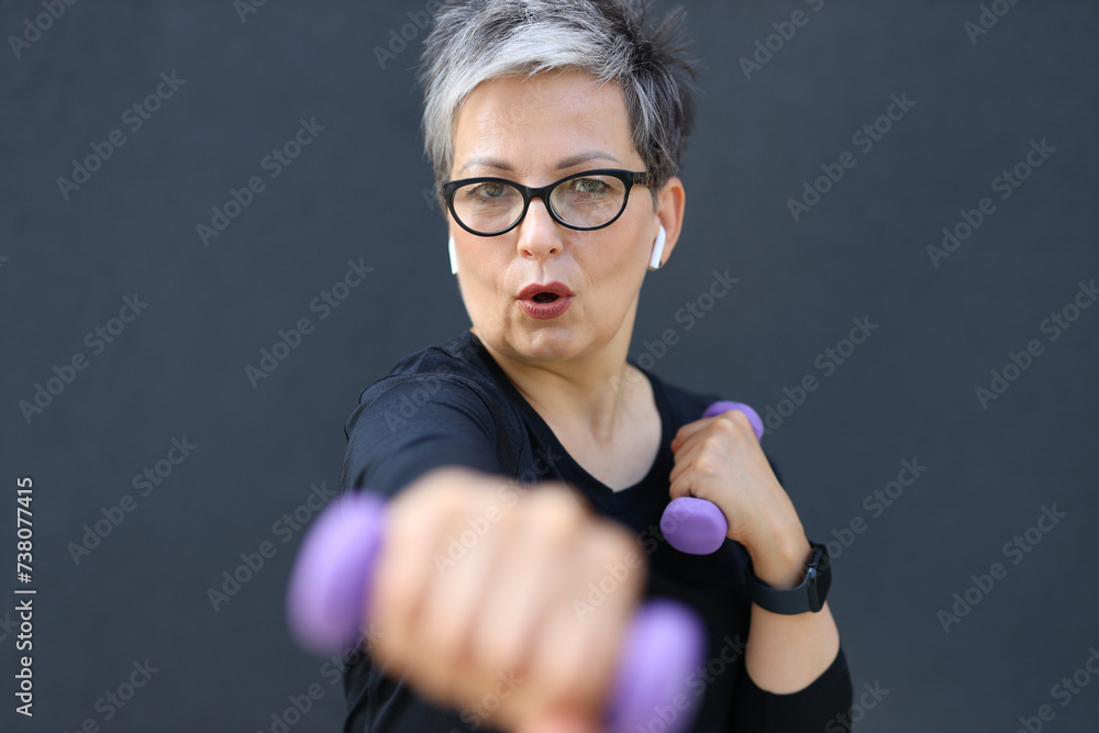 Sticker a mature caucasian woman stays fit and active, exercising with dumbbells in a gym studio.