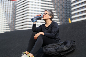 A healthy Caucasian woman takes a break in the park, staying hydrated with a refreshing water bottle.