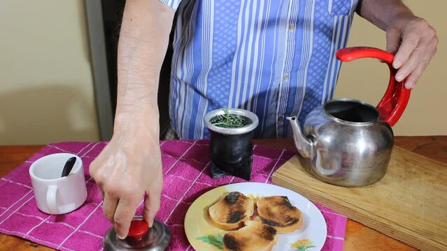 Tradiciones del t&eacute; verde oriental y sudamericano, el hombre prepara el t&eacute; de la tarde en la mesa con los pocillos blancos y coloca la hierba en la tetera, con el pan tostado en el plato