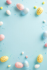 Delightful festivity vibes. Vertical top view of empty surface surrounded by sugar sprinkles and cheerful eggs atop pastel blue surface. Ample space for your heartfelt messages or promotional content