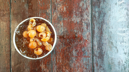 Longan drink with fresh fruit peel the skin show white meat and black seed on a wooden background.