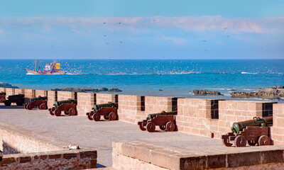 Fishing boat loaded by fishes in its back is being followed by seagulls - ESSAOUIRA, MOROCCO - Citywall Scala de la Kasbah with cannons, View to Fortress Scala du Port - Historic city Medina 