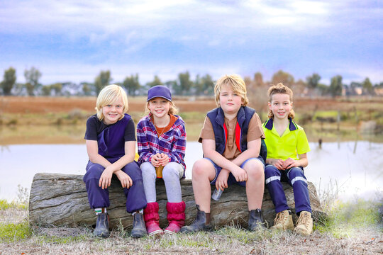 Group of happy country kids sitting on log on farm with dam in background