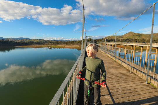 Child riding scooter on the Rail Trail bridge crossing over Lake Eildon from Bonnie Doon
