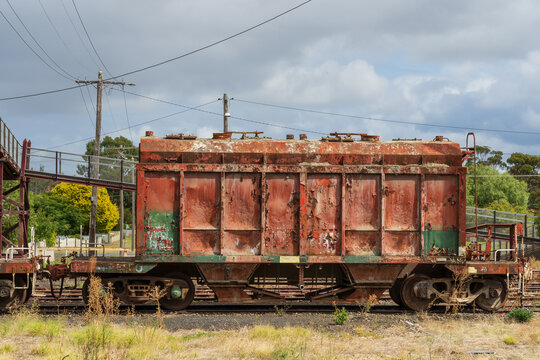A rusty red railway carriage sitting on tracks under a cloudy sky