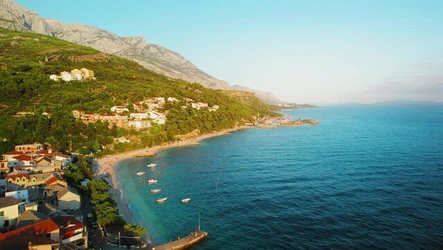 Seaside village at sunset golden hour in summer Croatia. The coastal town nestles against the rugged slopes of Biokovo mountain. Makarska Riviera and Adriatic Sea.