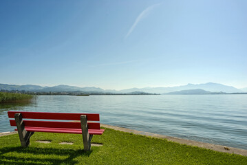 Zwei rote Sitzbänke am Zürichsee mit Sicht auf die Alpen