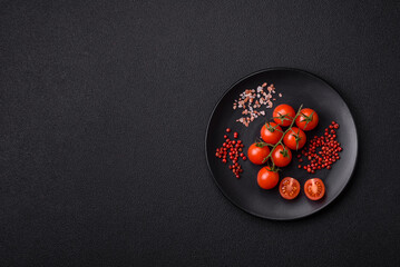 A branch of raw cherry tomatoes with salt and spices on a dark background