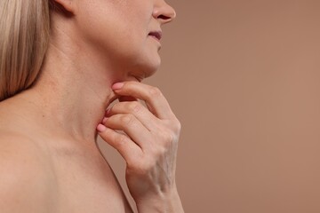 Fototapeta na wymiar Mature woman touching her neck on beige background, closeup. Space for text