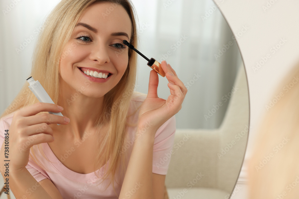 Wall mural Beautiful woman applying mascara near mirror at home