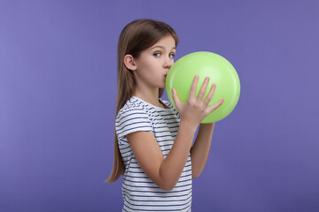 Girl inflating light green balloon on violet background