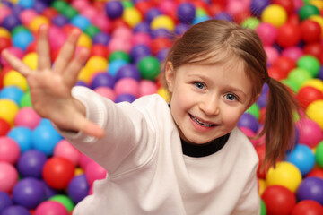 Fototapeta na wymiar Happy little girl sitting on colorful balls in ball pit