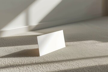 White business card standing on soft carpet with dynamic shadows.