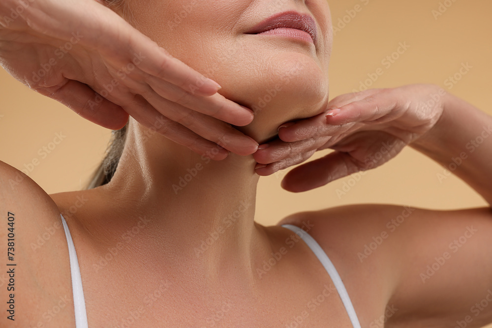 Poster Mature woman touching her neck on beige background, closeup