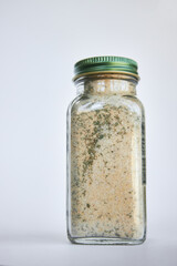 Glass jar with loose dried mixture close-up. Using reusable, recyclable Eco-friendly packaging in everyday life. Organic Seasoning Blend mix. Gray background. 