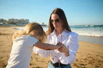 Mom and daughter holding hands while playing together on the beach on warm sunny day