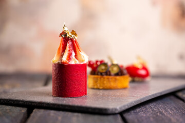 Three fancy desserts with berries on a gray slate board against a mottled pink background
