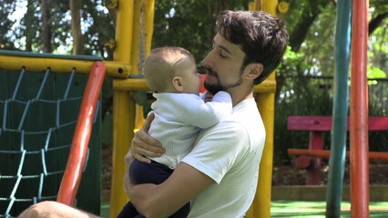 Fototapeta premium Father holding baby son outside at playground park embracing and loving