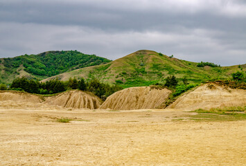 Landscape of a serene field surrounded by rolling hills, beneath a cloudy sky