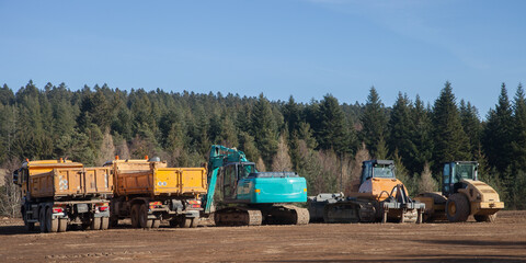 Panorama sur plusieurs engins de chantier : camions, pelle mécanique, niveleuse