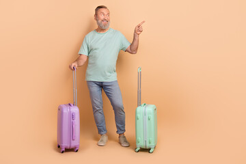 Full length photo of positive aged man hold suitcase look direct finger empty space offer isolated on beige color background