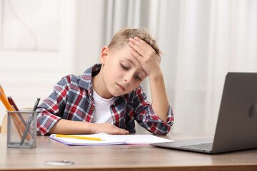 Naklejka premium Little boy suffering from headache at wooden desk indoors