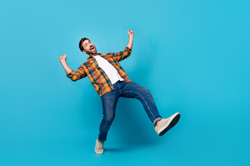 Fototapeta na wymiar Full size photo of handsome young male dance raise fists cheerful dressed stylish checkered outfit isolated on blue color background