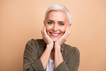 Close up portrait of cheerful white short hair lady in khaki shirt touch cheeks admiring and...