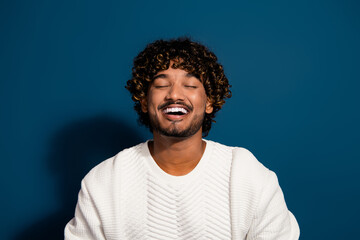 Portrait of young funny guy in white jumper curly hair student from mexico laughing closed eyes isolated on dark blue color background