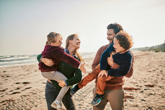 Family enjoying time together on the beach with parents carrying children