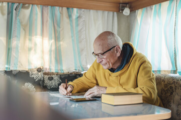 Senior man at table writing words in crossword with pencil and reading notes in smartphone in style...