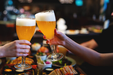 Two friends woman hands clinking glasses of craft beer at the pub or bar