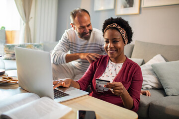 Diverse middle aged couple using laptop for online shopping at home