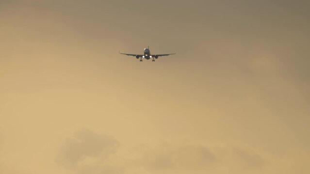 Footage of a jet plane approaching landing. Passenger airliner flies in the sunset sky, front view, long shot