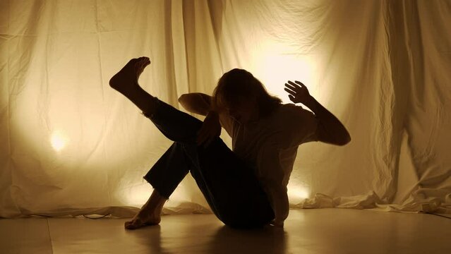 Silhouette contemporary experimental choreography concept. Female dancer performing in the studio. Young girl dancing against warm back light