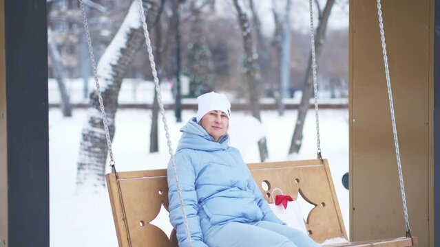 Young woman relaxing ang swinging on swings in winter in park near. 