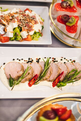 Fragment of buffet table with plates of meat, cheese slices, cold vegetable salads, sweet desserts.