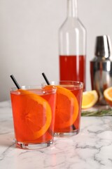 Aperol spritz cocktail, orange slices and straws in glasses on white marble table