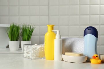 Baby cosmetic products, bath duck, cotton swabs and towel on white table against tiled wall