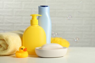 Baby cosmetic products, bath duck, sponge and towel on white table against soap bubbles. Space for text