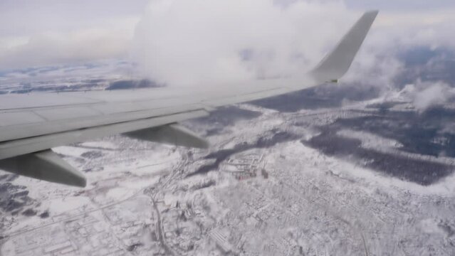 View of snowy landscape under the plane wing through plane porthole. White snow covered space and bright blue sky. Plane engine and winglet as seen from cabin